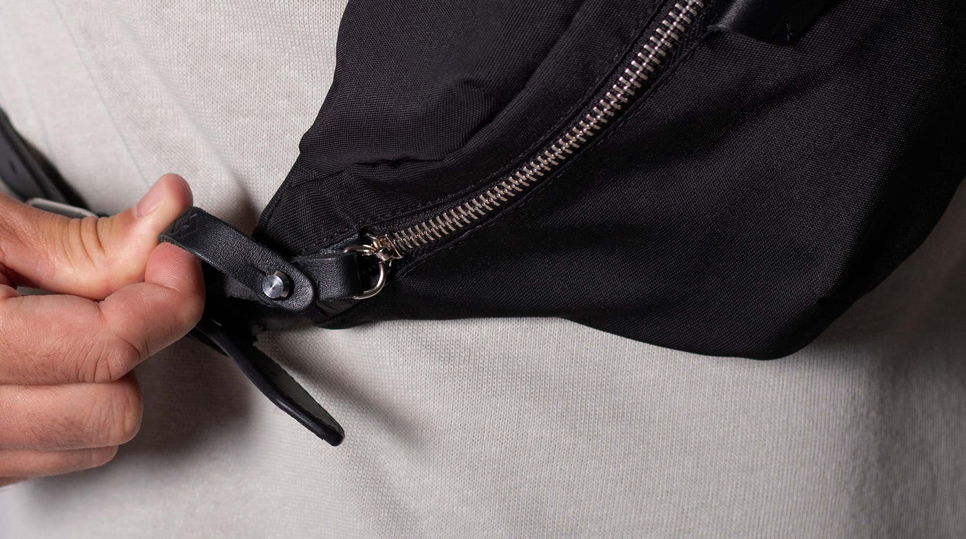 Person opening a black crossbody bag with a zipper 