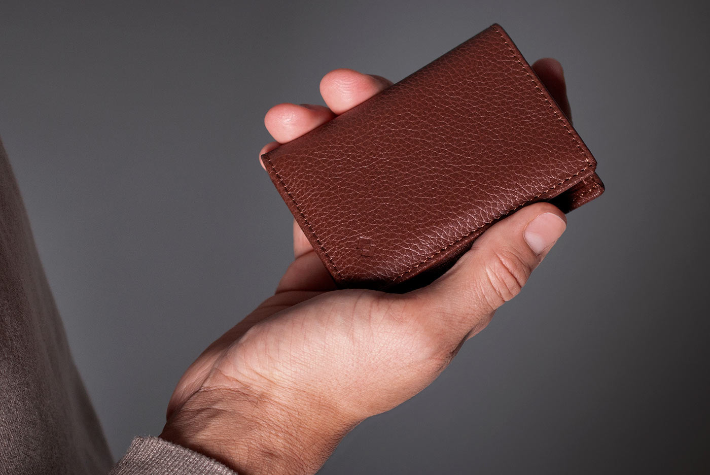 Hand holding a brown leather wallet against a gray background